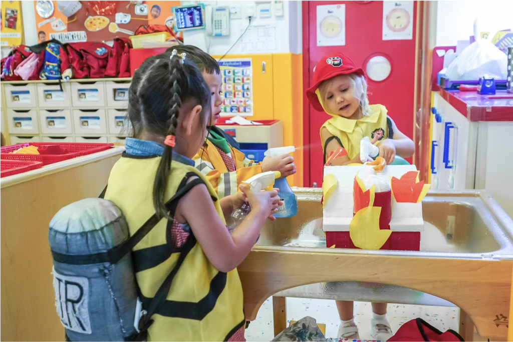 Children are learning about occupations by dressing up as firefighters and ‘putting out’ the fire with their teammates