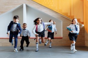 Primary schoolchildren in uniforms running joyfully in a corridor